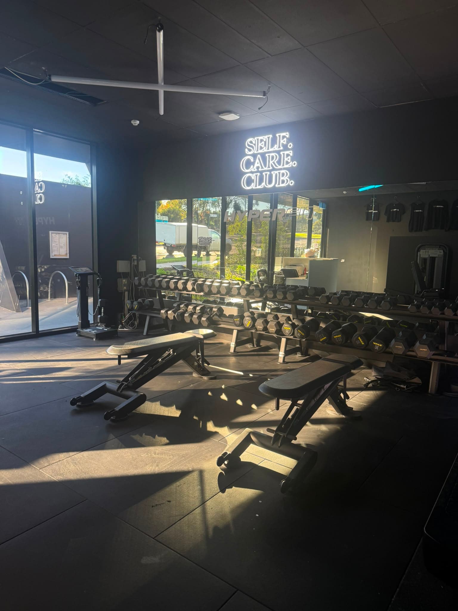 Dumbbell racks and benches with Self Care Club neon sign
